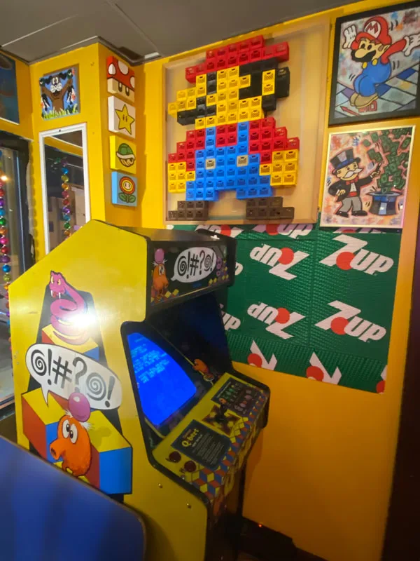 Q*bert arcade cabinet beside a Lego Mario mosaic and a 7UP Lego wall inside Happy Dough Lucky