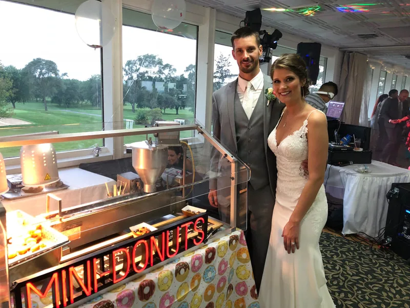 Bride and groom standing beside the neon mini donut bar at their wedding reception