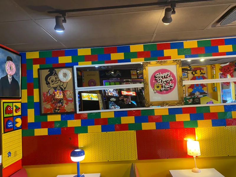 Lego-brick wall with a gold-framed Happy Dough Lucky logo above yellow booths and table lamps